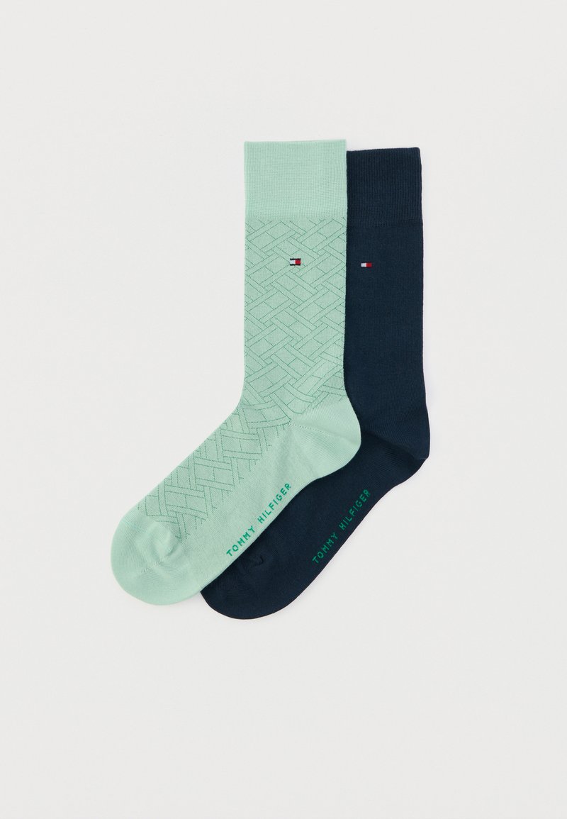 Κάλτσες σε μέντα πράσινο και σκούρο ναυτικό μπλε· η μία διαθέτει γεωμετρικό σχέδιο, η άλλη είναι μονόχρωμη. Και οι δύο έχουν το λογότυπο «Tommy Hilfiger» σε πράσινο.