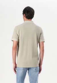 Lys beige polo skjorte med korte ermer, flat krage og en glatt tekstur, kombinert med lyseblå jeans. Minimalistisk design.