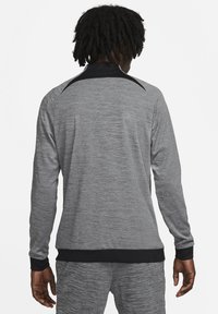 Gray athletic long-sleeve pullover with a textured finish. Features a black collar and cuffs, with a snug hem. No visible logos or patterns.