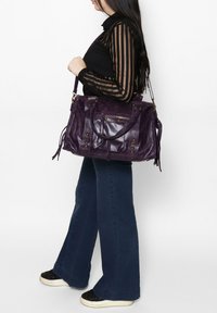 Sac à main en cuir violet avec surface texturée, plusieurs poches zippées et bretelles réglables ; des accents de gland ajoutent du d�étail.