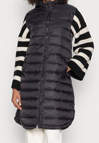 Czarna kurtka puchowa zapinana na zamek z kapturem. Rękawy z dzianiny w paski w kolorze czarnym i kremowym. Teksturowany, ciepły i sięgający do kolan fason.