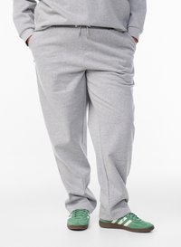 Pantalon de jogging gris en tissu doux, avec une taille élastique munie d'un cordon de serrage et des poches latérales ; assorti à des baskets vertes.