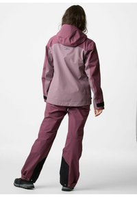 Completo outdoor da donna a due pezzi in sfumatura viola, composto da giacca con cappuccio, polsini elasticizzati e pantaloni ventilati con dettagli neri.