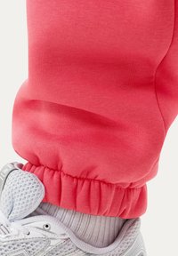 Rød bukseben med elastisk manchet over hvid sportssko med mesh-design og hvid ribbet sok synlig over skokraven.