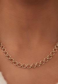 Collier chaîne en or avec des maillons ronds entrelacés porté autour du cou d'une personne à la peau brune.