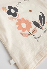 Baumwoll-Tragetasche mit floralem Design in Schwarz, Pfirsich und Weiß. Verziert mit handgezeichneten Blumen und dem Text "daisy chain" mit strukturierter Oberfläche.