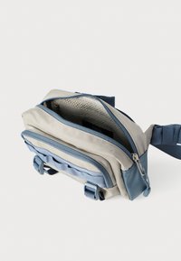 Τσαντάκι ώμου από ύφασμα σε μπεζ και μπλε χρώμα, με πολλαπλές θήκες, κλείσιμο με φερμουάρ και ρυθμιζόμενο λουρί για ασφαλή μεταφορά.
