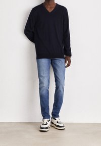 Marinblå v-ringad tröja, lätt material. Slim-fit ljusblå jeans. Multifärgade sneakers med svarta accenter och vit sula. Enkel, modern stil.