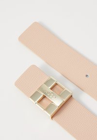 Lichtroze leren riem met textuur, voorzien van een rechthoekige goudkleurige gesp met een reliëflogo. Inclusief een klein metalen sluitdetail.