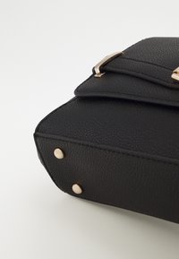 Borsa nera in pelle sintetica con superficie testurizzata, dettagli in metallo dorato e borchie metalliche alla base per stabilità.