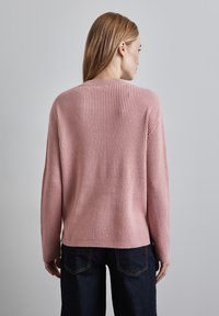 Rosa gerippter Pullover mit lockerem Schnitt und langen Ärmeln, verfügt über einen Rundhalsausschnitt und reicht bis zur Hüfte, kombiniert mit dunklen Jeans.