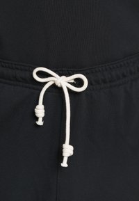 Fascia elastica nera con un cordino bianco annodato a fiocco, con dettagli di cucitura visibili e una texture liscia.