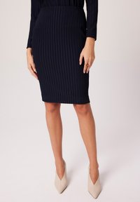 Granatowa spódnica ołówkowa w prążki wykonana z gładkiego materiału, sięgająca tuż nad kolano. Zestawiona z jasnobeżowymi szpilkami w szpic.