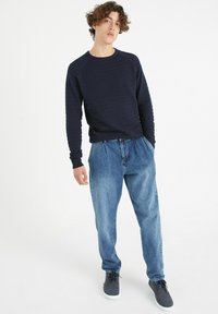 Camisa de manga larga texturizada en azul marino combinada con pantalones de mezclilla sueltos de color azul claro y zapatillas oscuras. Un conjunto sencillo y casual con un ajuste relajado.