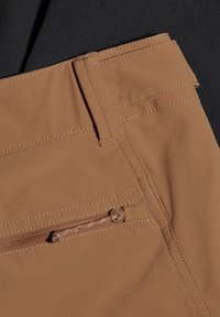 Bruine broek met een gladde textuur, voorzien van schuin geplaatste zakken en een zijrits. Contrasterende stikseldetails versterken het ontwerp.