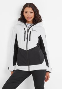 White and black ski jacket featuring a chevron design, zippered front pockets, adjustable cuffs, and a hood. Smooth, water-resistant material.