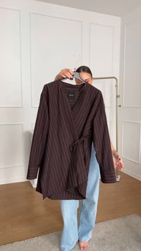 Brown wrap top with white vertical stripes, made of a smooth fabric. Features a V-neckline, long sleeves, and a tied waist detail.
