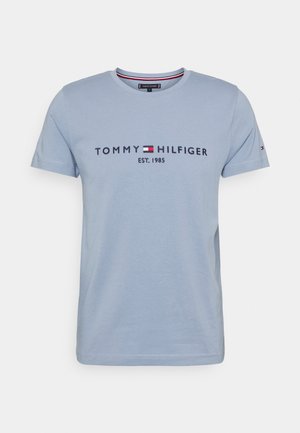 Jasnoniebieska koszulka z krótkim rękawem z napisem "Tommy Hilfiger EST. 1985" oraz czerwono-biało-niebieskim logo na przedniej części klatki piersiowej.