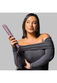 Remington hårglatter i mauve, slank design med en lang strømkabel, holdt av en person som har på seg en grå avskjærmingsgenser.