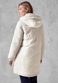 Lichtbeige pufferjack met een gemêleerde crèmekleurige capuchonvoering, elastische manchetten, een iets langere achterkant en minimalistische ontwerpdetails.