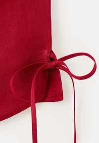 Coin de tissu en lin rouge avec un nœud attaché fait de fines lanières de tissu sur fond blanc.