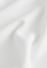 Tissu blanc texturé avec des plis doux, présentant une surface lisse et uniforme. Légèrement tissé avec un motif subtil, créant une apparence douce.