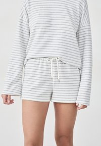 Biały zestaw wypoczynkowy z polaru z szarymi poziomymi paskami, składający się z luźnej bluzki z długim rękawem oraz szortów z regulowanym sznurkiem.
