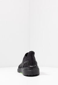 Czarny but sportowy z teksturowaną podeszwą i wsparciem pięty, przedstawiony z tyłu na białej minimalistycznej powierzchni.