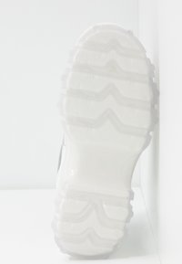 Semelle d'une basket blanche translucide avec un motif ondulé, photographiée par-dessous sur fond blanc.
