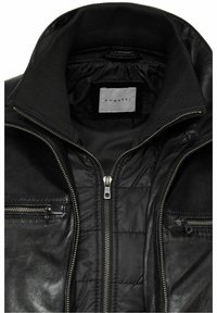 Chaqueta de cuero negra con cuello alto, presenta cremalleras plateadas y un interior acolchado. La etiqueta interior dice "bugatti."