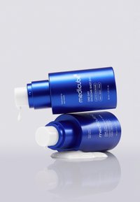 Due bottiglie di prodotti per la cura della pelle blu con pompe bianche, una in posizione verticale e una inclinata, che erogano un prodotto cremoso. Entrambe etichettate "medicube" con dettagli del prodotto.