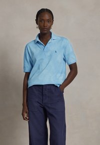Světle modré tie-dye polo tričko s límečkem a krátkým rukávem, doplněné o tmavě modré široké kalhoty s předními kapsami.