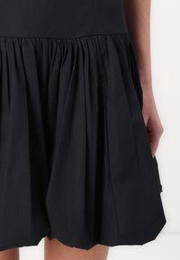 Jupe plissée noire en tissu léger, dotée d'une taille froncée et d'une silhouette évasée avec une texture lisse.