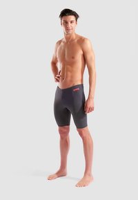 Herren-Badeshorts in Dunkelgrau mit glatter Textur. Verfügen über ein oranges Logo am Bund, entwickelt für Leistung und Komfort.