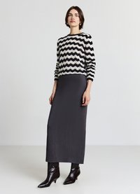 Pull en tricot à motif zigzag noir et blanc, associé à une jupe longue unie gris foncé et des bottines noires brillantes.