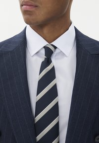 Jūrinis dryžuotas švarkas su balta marškinėliais ir jūriniu kaklaraiščiu su šviesiomis juostelėmis. Lygus audinys ir klasikinis apykaklė.