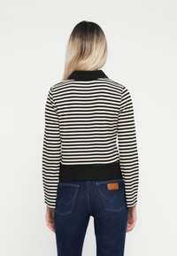 Striped sweater in black and white with a ribbed collar and cuffs, featuring long sleeves and a fitted silhouette. Worn with dark denim jeans.