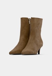 Bottines en daim marron à bout pointu et talon fin, avec une fermeture éclair latérale et une texture douce. Design élégant et ajusté.