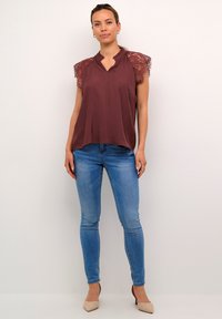 Bordeaux topp med spetskortärmar, v-ringning, i kombination med slim-fit blåjeans och beige klackar. Slät tyg med texturerade spetstillägg.
