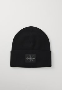 Zwarte gebreide beanie met opgerolde rand, voorzien van een zwart label met het 'Calvin Klein' logo in grijs en witte letters.