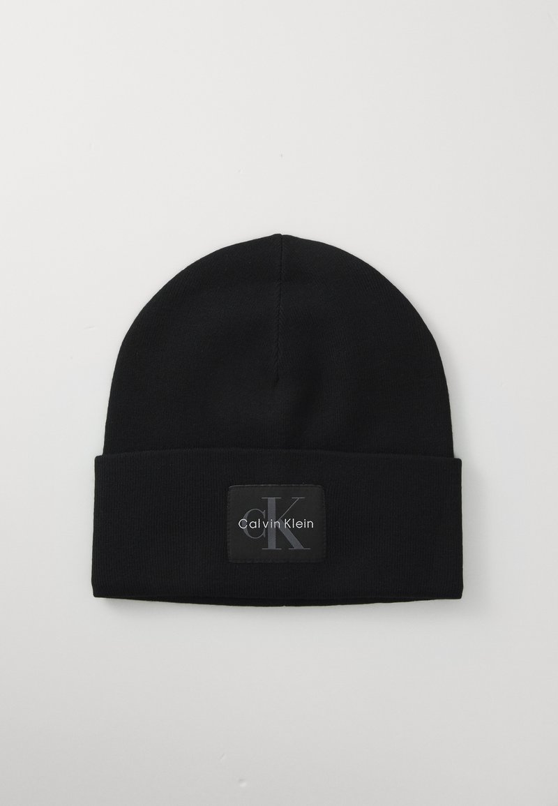 Zwarte gebreide beanie met opgerolde rand, voorzien van een zwart label met het 'Calvin Klein' logo in grijs en witte letters.