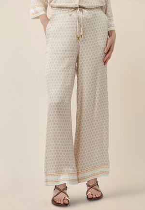 Beige Hosen mit weitem Bein und leichtem Polka-Dot-Muster, Tunnelzug am Bund und umgeschlagenen Säumen, getragen mit braunen Riemchensandalen.