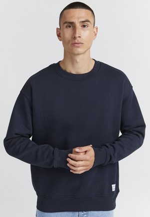 Marineblauwe sweatshirt met een ronde hals, lange mouwen, zachte textuur, geribbelde manchetten en zoom, voorzien van een klein label aan de onderlinkerzijde.