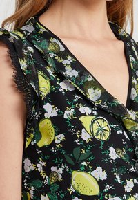 Svart tyg topp med ett blommönster som har citroner och grönska. Urrigningen är v-formad med spetsdetaljer.