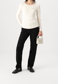 Top de manga larga de canalé crema, pantalones rectos negros y un bolso pequeño blanco. La modelo lleva zapatos negros sin cordones. Estilo minimalista.