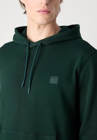 Felpa verde in misto cotone, con tasca frontale, coulisse regolabili e una toppa quadrata con logo sul petto.