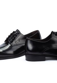 Zapatos de vestir de cuero negro con textura suave, diseño con cordones y un sutil logo en el lateral. Presentan una punta redondeada y un tacón bajo.