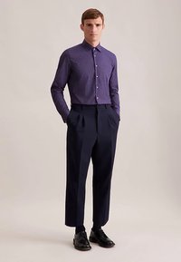 Paarse overhemd met knopen en een klein geometrisch patroon, gecombineerd met hoogtaillistische marineblauwe broek en zwarte lederen schoenen.