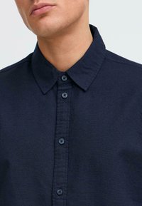 Camisa azul marino de botones con cuello clásico, tejido texturizado y botones en contraste, que muestra un aspecto limpio y bien ajustado.
