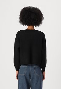 Suéter negro de punto con un ajuste relajado, cuello redondeado y mangas largas ligeramente abullonadas. Combinado con jeans azul de cintura alta.